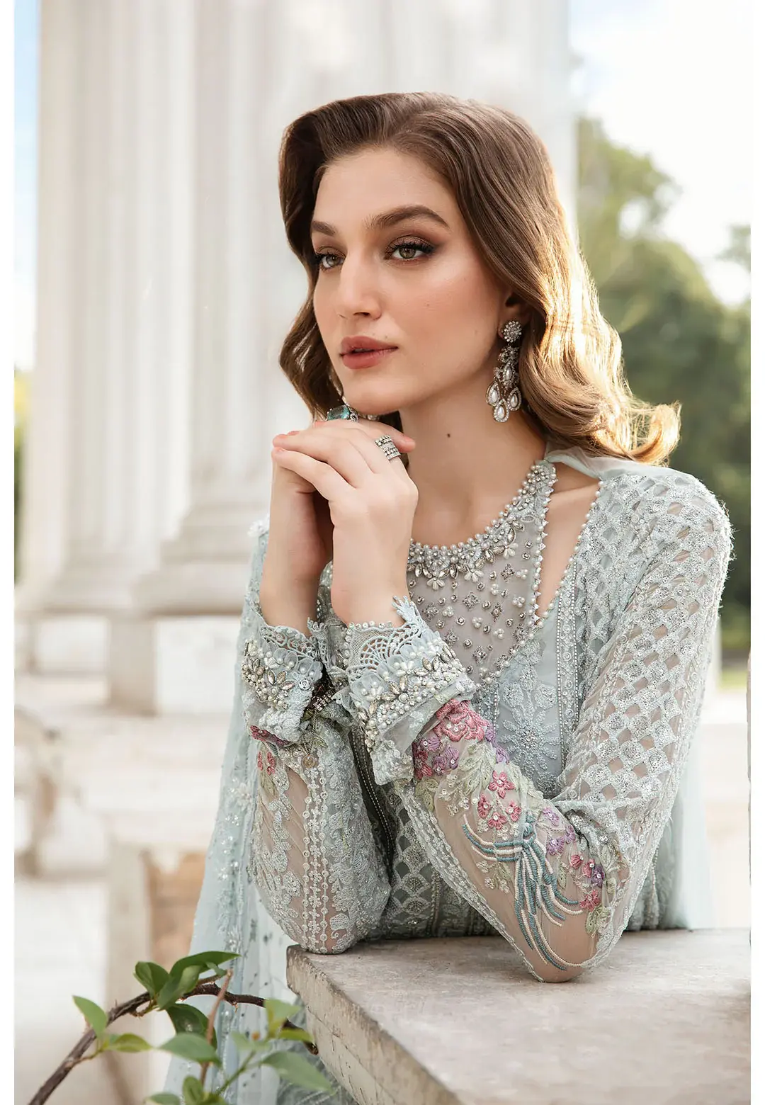 457000776_984541653713099_304138683664589485_n_1800x1800-1.webp A model in a pastel blue embroidered outfit with intricate floral detailing, gracefully posing in front of white neoclassical columns.