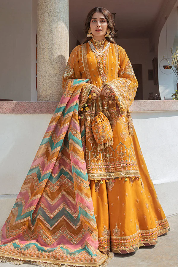 heenna A woman in a vibrant, embellished mustard-yellow Pakistani lehenga with a colorful chevron dupatta and a matching pouch. The image highlights the intricate details and bright aesthetic of the mehndi dresses for girls.